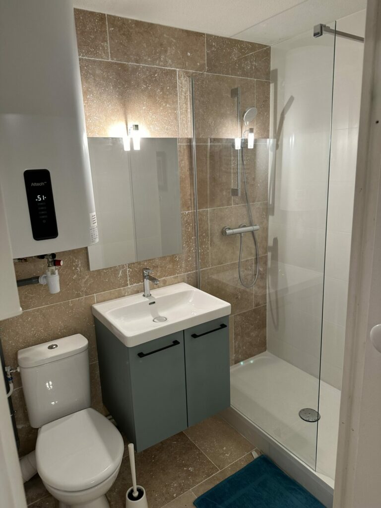 Image d'une salle de bain moderne avec douche en verre, lavabo sur meuble gris et toilettes, conçue par Al'Eau Nico.